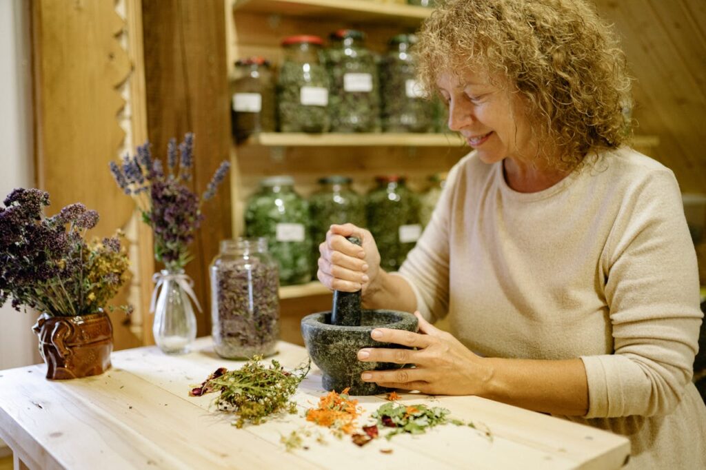 A woman uses a mortar and pestle to prepare natural herbal remedies indoors.